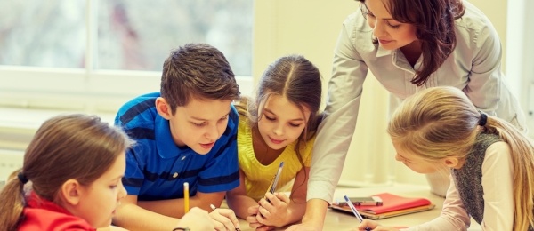 An instructor working with a group of elementary school students around a table.