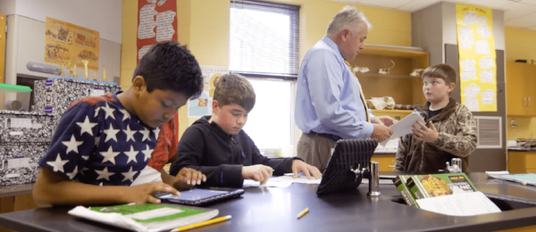 Students working independently in a classroom, as an instructor collects assignments.