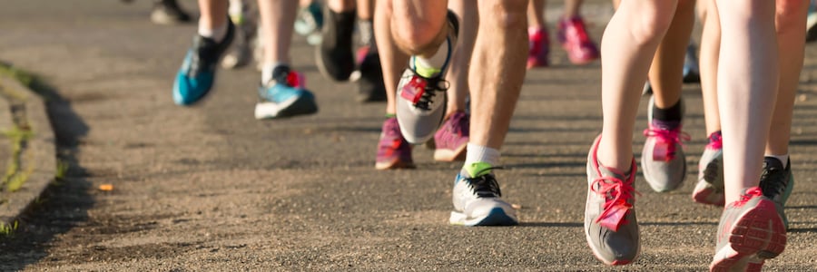 Multiple people wearing shorts and sneakers or running shoes running in a road race.