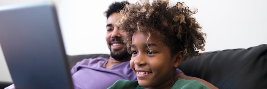An older black male and a young black child smile together at an electronic tablet. Families and Distance Learning: A Guardian’s Guide To Kicking Off Distance Learning