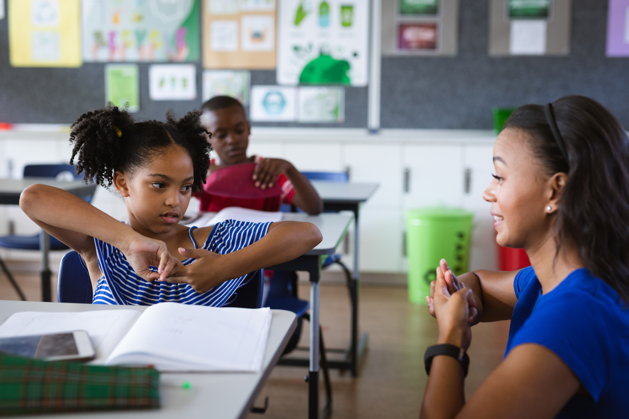 African american female teacher and a girl talking in hand sign language at elementary school